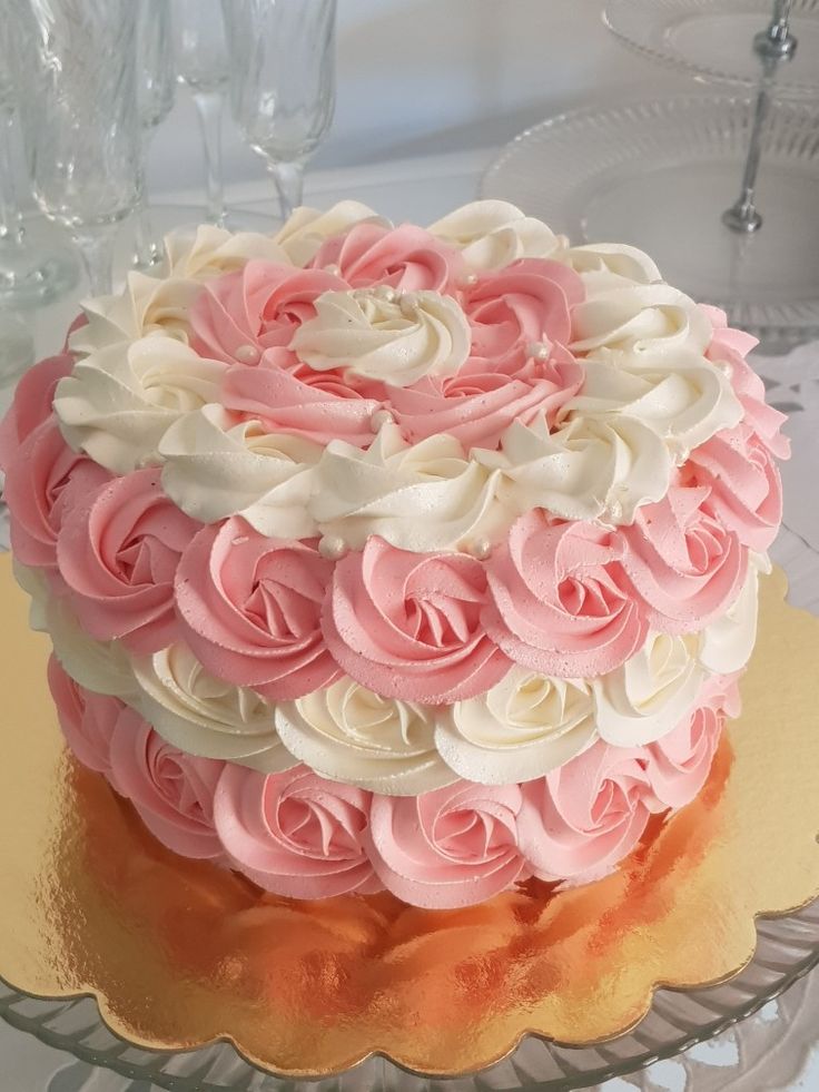 a cake with pink and white frosting roses on it sitting on a glass platter