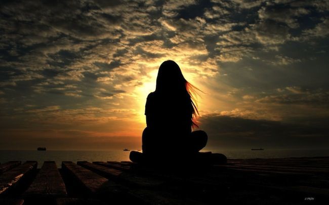 the silhouette of a woman sitting on a dock at sunset