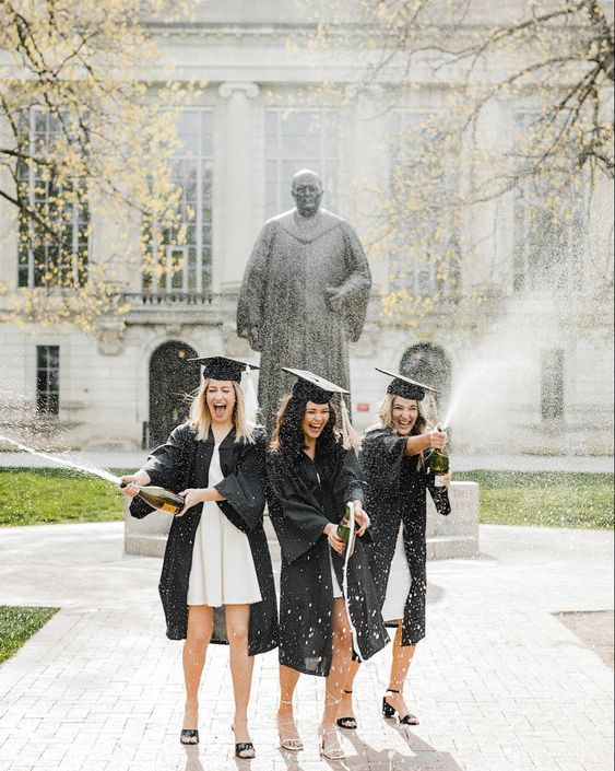 three women in graduation gowns and hats are throwing water at each other with their hands