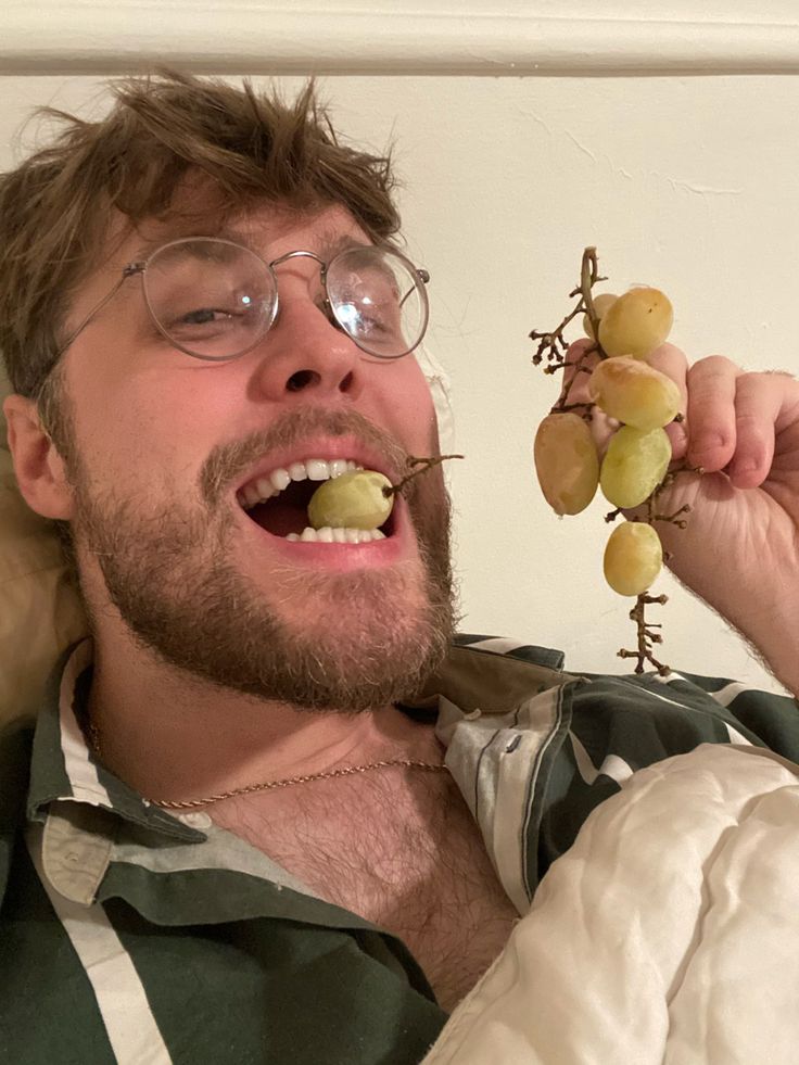 a man with glasses is holding grapes in his hand and looking up at the camera