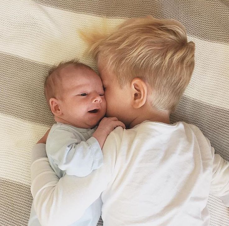 a baby laying on top of a bed next to an adult holding it's head