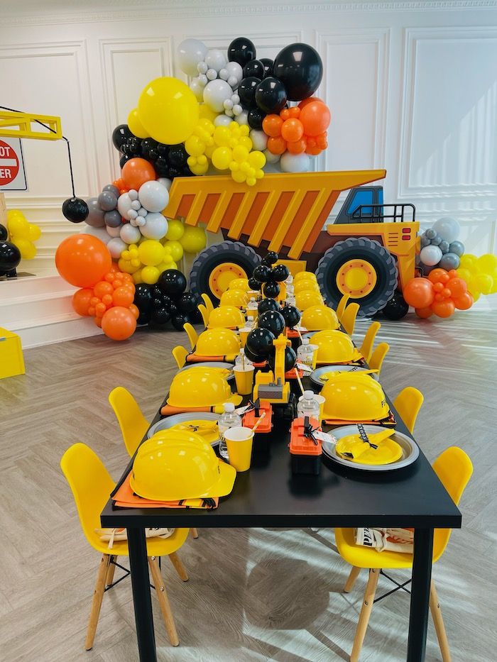 a construction themed party with yellow chairs and black table cloths, balloons and decorations