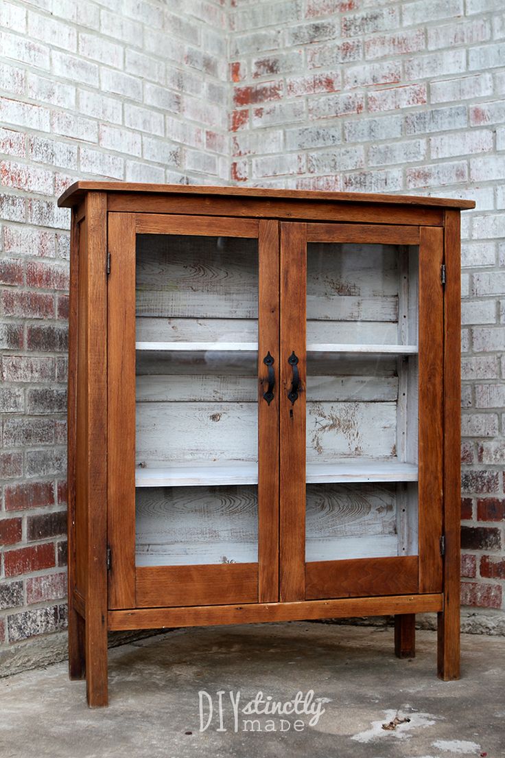 an old wooden cabinet with glass doors on the top and bottom, against a brick wall