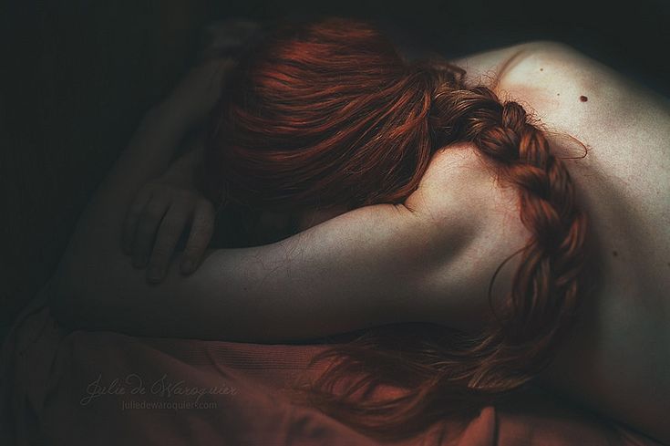 a woman with red hair laying on top of a bed next to her head and body