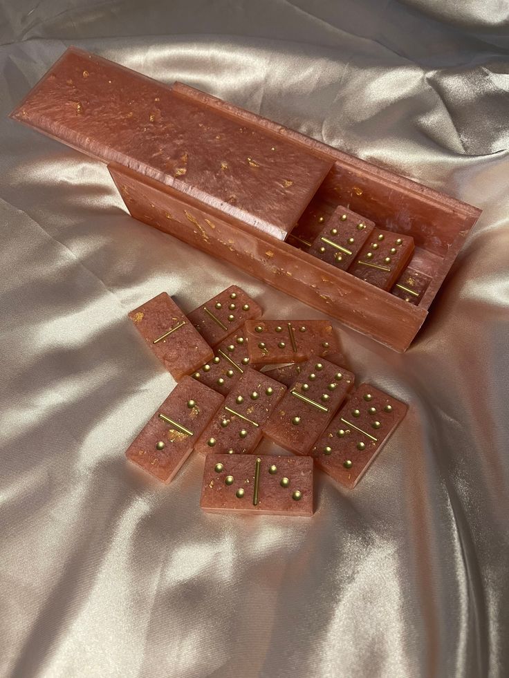 a wooden box filled with chocolate pieces on top of a satin covered table cloth next to it