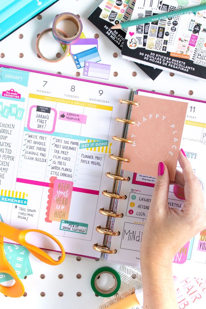 a person holding a planner in their hand next to some scissors and other items on a table