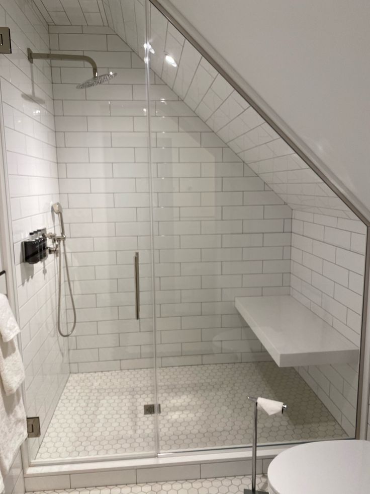 a bathroom with a walk in shower next to a white toilet and sink under a slanted ceiling