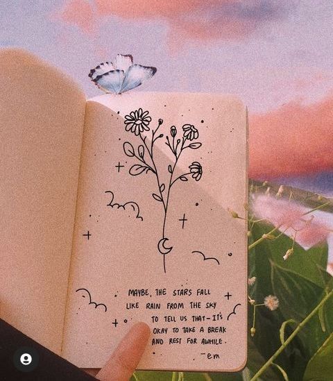 a hand holding an open book with a drawing on the pages and a butterfly flying over it