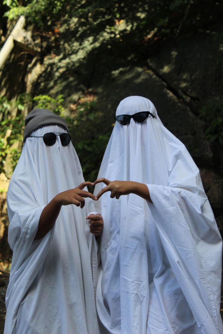 two people dressed in white standing next to each other with their hands forming the shape of a heart