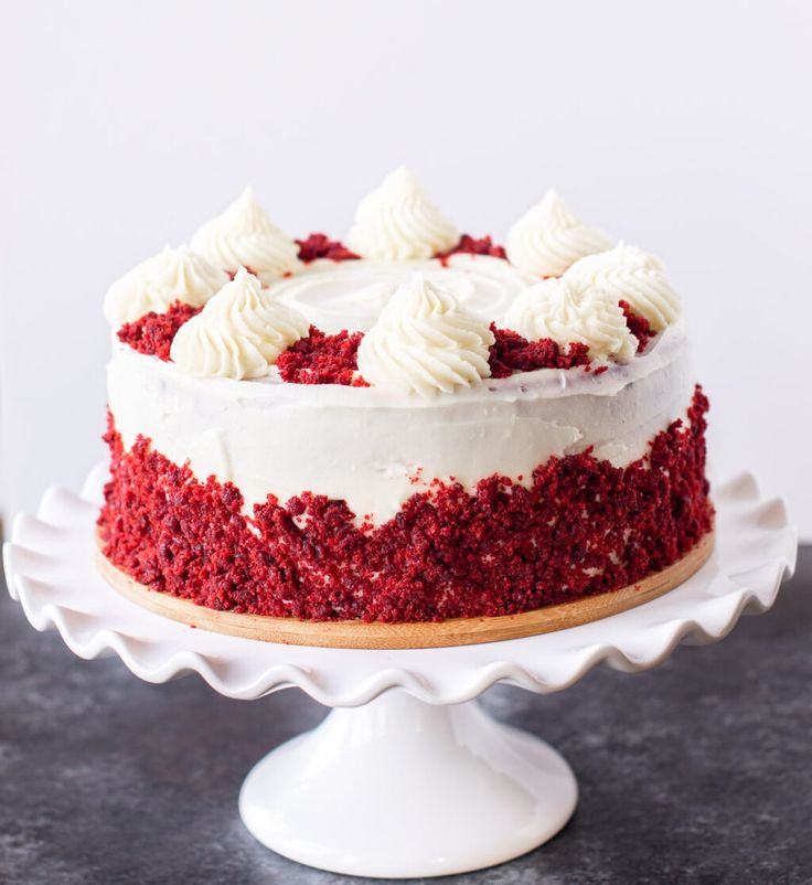 a red velvet cake with white frosting on a pedestal, ready to be eaten