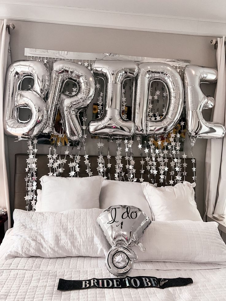 a bed with white sheets and silver balloons