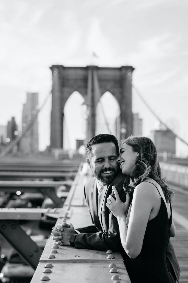 a man and woman standing next to each other in front of a bridge with the brooklyn bridge in the background