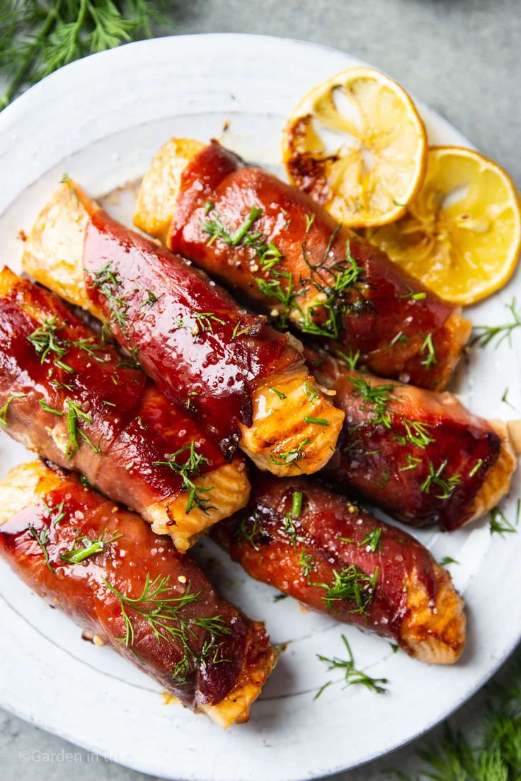 chicken wrapped in bacon and garnished with herbs on a white plate next to lemon wedges