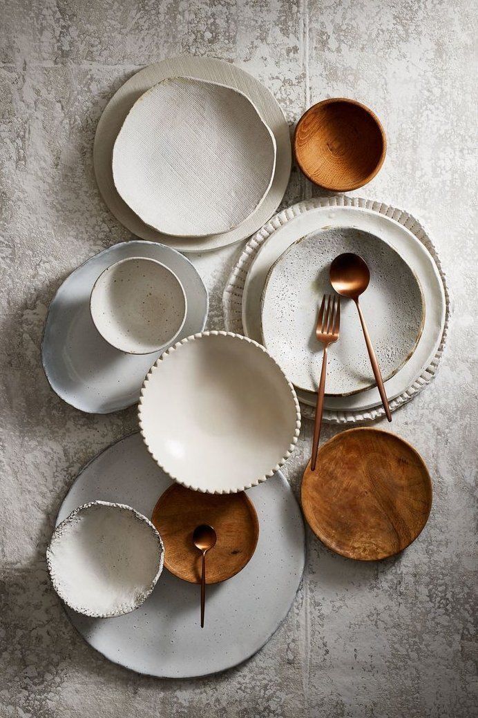 a table topped with white plates and silverware next to wooden spoons on top of each other