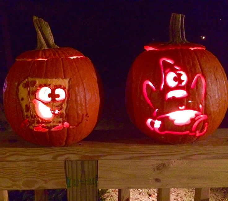 two pumpkins with faces carved into them sitting on a wooden porch railing at night