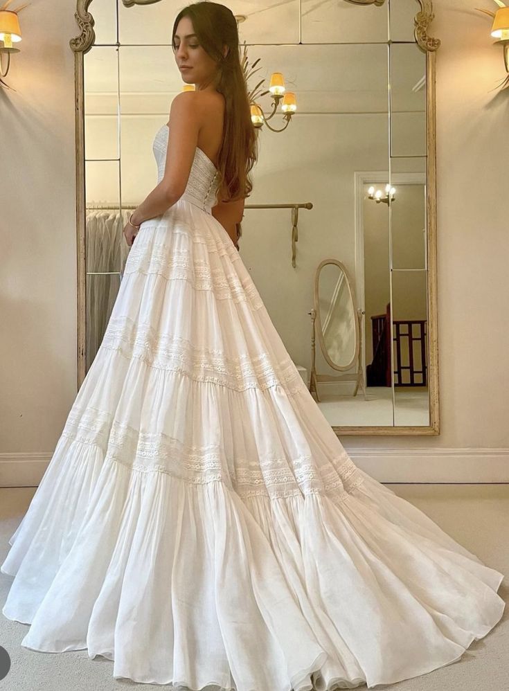 a woman standing in front of a mirror wearing a wedding dress with tiered ruffles