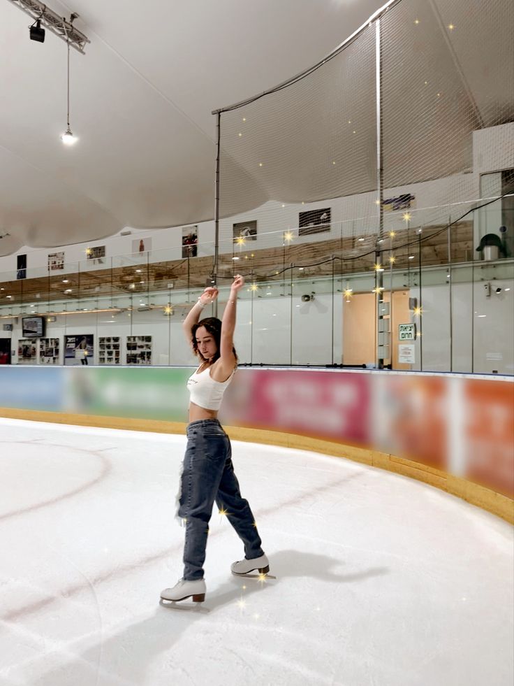 a woman standing on top of an ice rink holding her arms up in the air