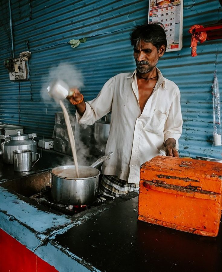 a man in white shirt cooking on stove top next to orange box and blue wall