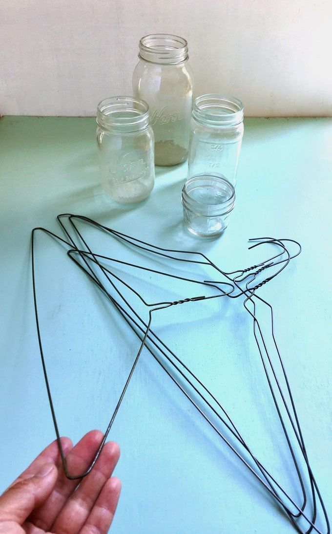 a hand is holding some wire on top of a table next to jars and mason jars