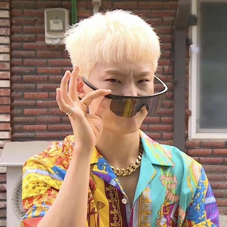 a young man with blonde hair and glasses covering his face while standing in front of a brick building