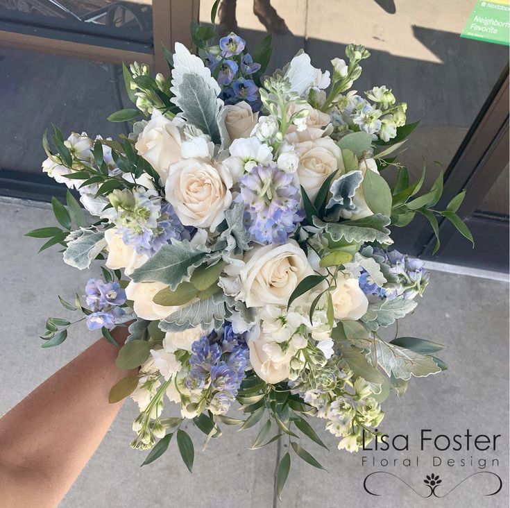 a bouquet of white and blue flowers is held by someone's hand in front of a door