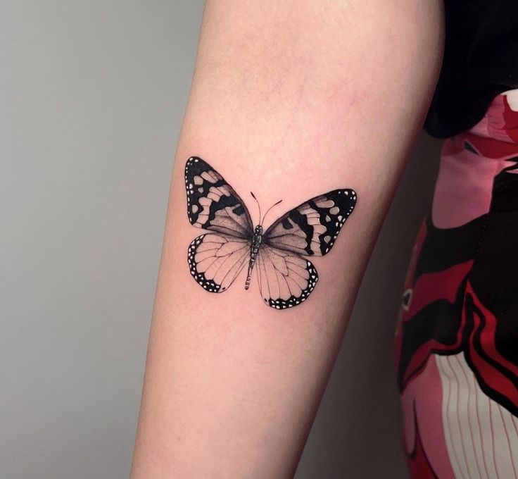 a black and white butterfly tattoo on the right arm by a woman's leg