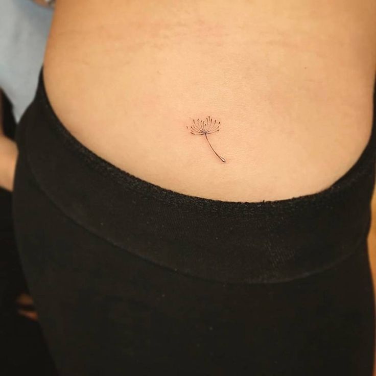 a woman's stomach with a small dandelion tattoo on her side belly