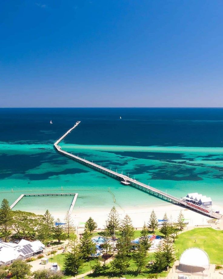 an aerial view of the beach and ocean with a pier in the foreground, surrounded by blue water