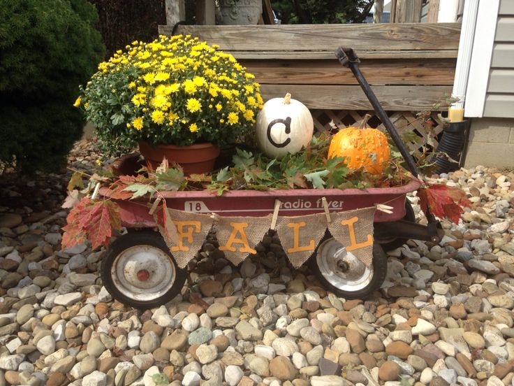 a wagon filled with plants and pumpkins sitting on top of a gravel covered ground