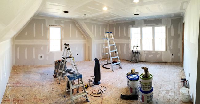 an unfinished room with ladders, paint cans and other tools on the floor in front of two windows