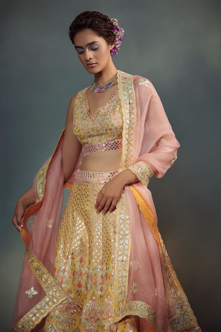 Yellow lehenga in raw silk embroidered with resham, gota, leather and mirror work. Paired with a co-ordinating embroidered V-neck blouse and contrast pink organza dupatta.
Component: 3
Embroidered
Neckline: V-Neck
Sleeve Length: Sleeveless
Fabric: 100 grams Pure Raw Silk, Organza; Lining: Cotton, Shantoon
Color: Yellow
Embroidered dupatta border with tassel edges
Back tassel tie-up blouse
Closure:
Blouse: Back closure with hook and tie-up
Lehenga: Side zip closure - Aza Fashions Raw Silk Embroidery, Dupatta Border, Raw Silk Lehenga, Yellow Lehenga, Embroidered Lehenga, Gold Blouse, Indian Wedding Wear, Embroidered Dupatta, Work Skirts