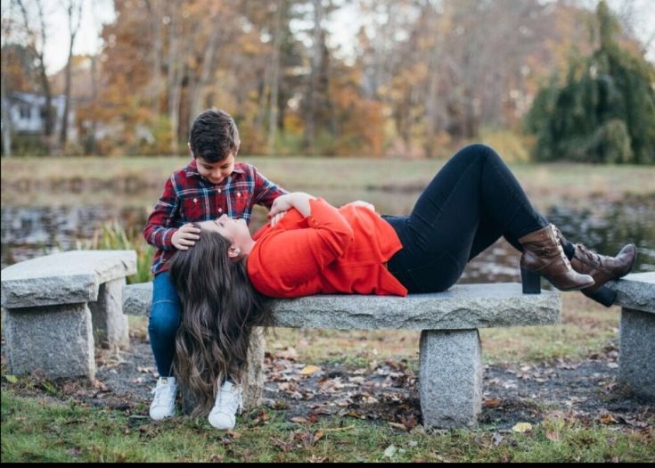 a man and woman sitting on a stone bench in the park with their heads touching each other