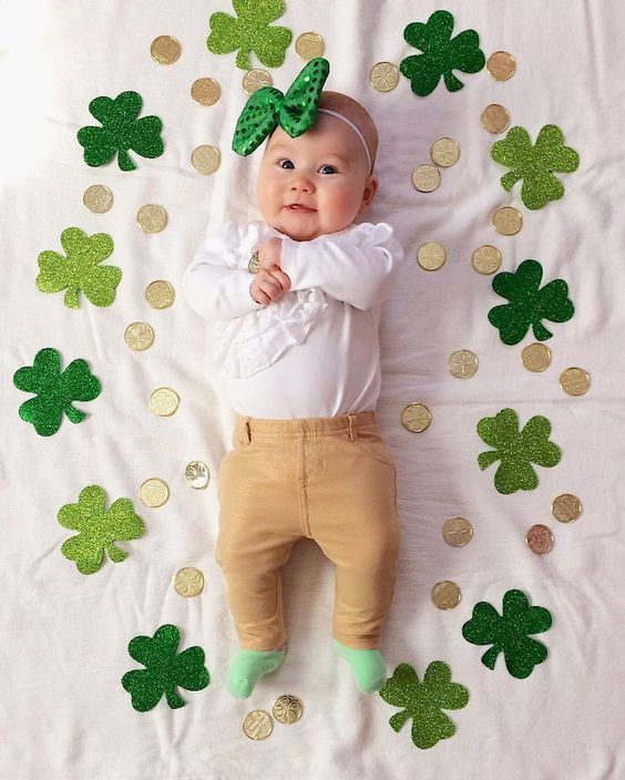 a baby laying on top of a bed with green shamrocks around it's head