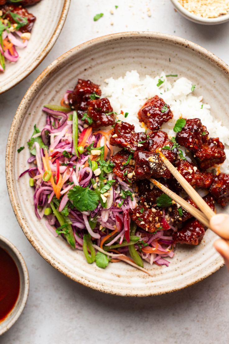 someone holding chopsticks over a bowl of food with rice and sauce on the side