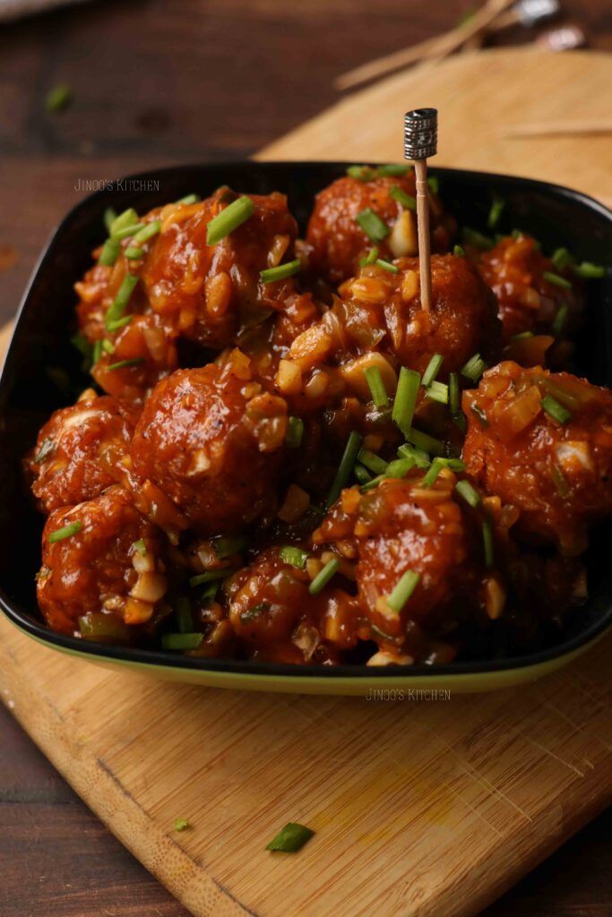 meatballs with green onions and sesame seeds in a black bowl on a wooden cutting board