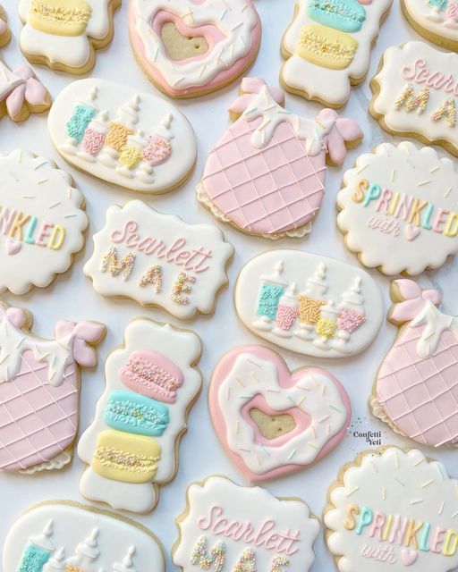 some decorated cookies are laying on a white tablecloth with the words sprinkled in pink, blue and yellow