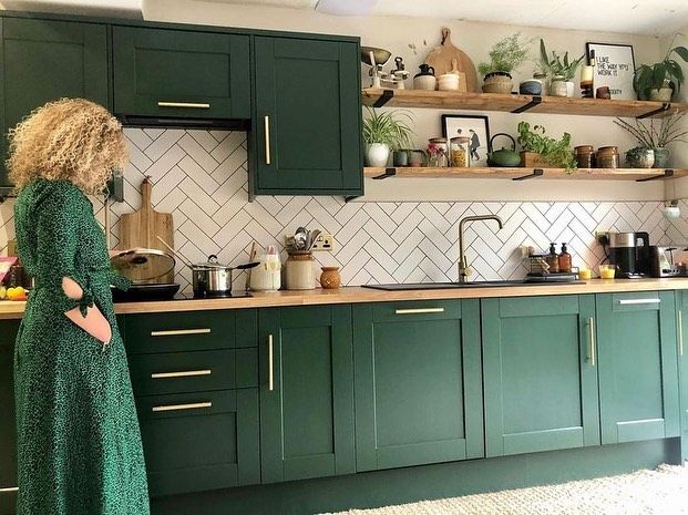 a woman in a green dress is looking at the kitchen cabinets and counter tops that are painted dark green