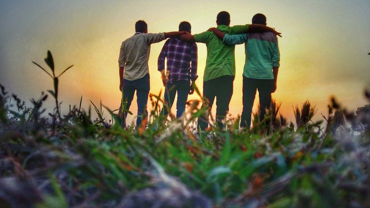 three people standing in the grass with their arms around each other as the sun sets