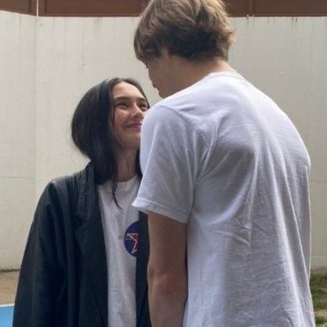 two young people standing next to each other near a basketball court, talking and smiling