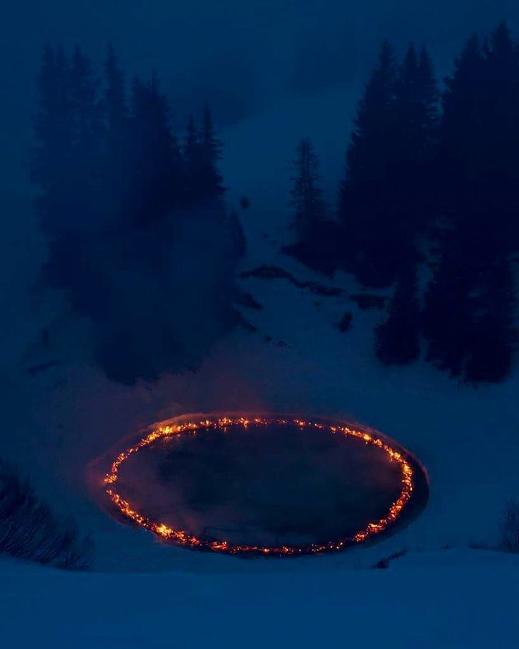 a circular fire pit in the middle of a snow covered field with trees around it