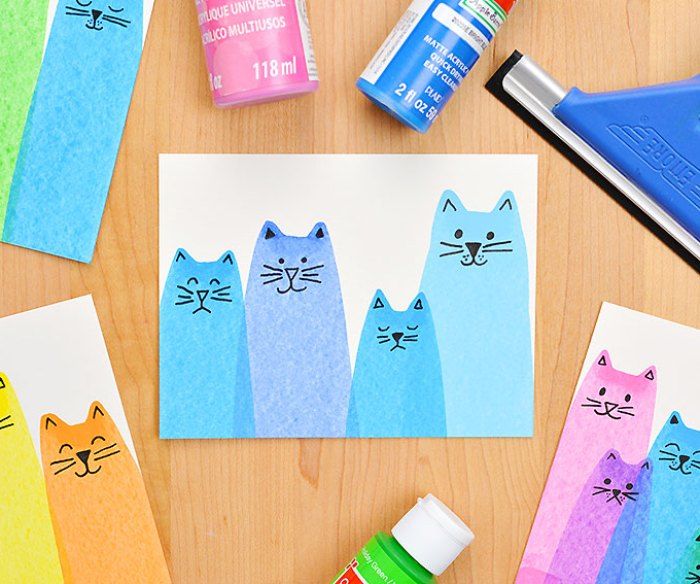 colorful paper cutouts with cats on them next to glue markers and watercolors