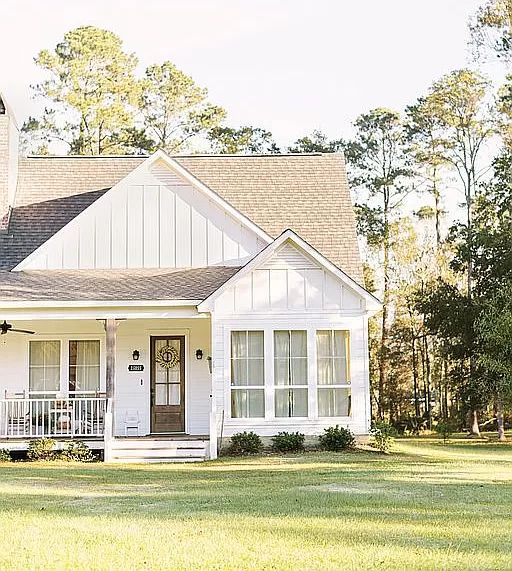 a white house in the middle of a grassy area with trees and bushes around it