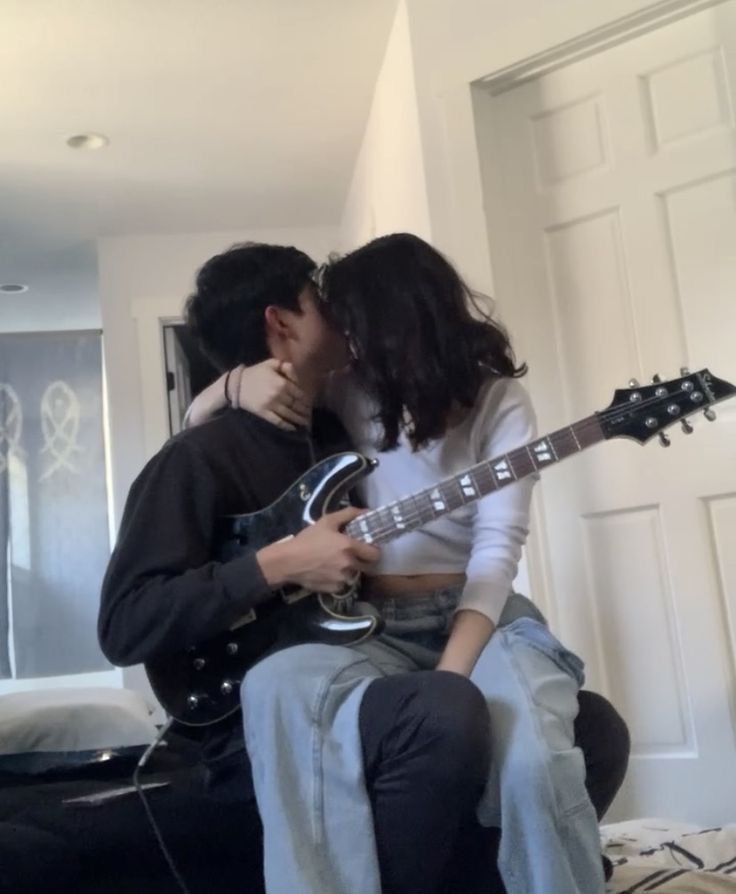 a man and woman kissing while holding an electric guitar