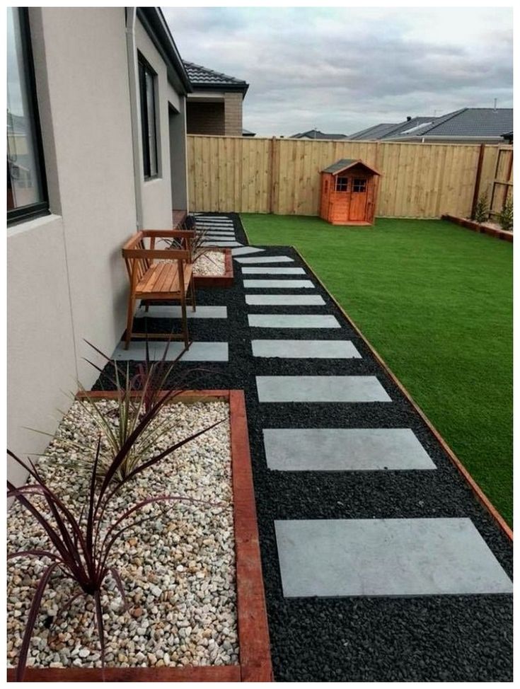 a small backyard with grass, gravel and wooden benches on the side of the house