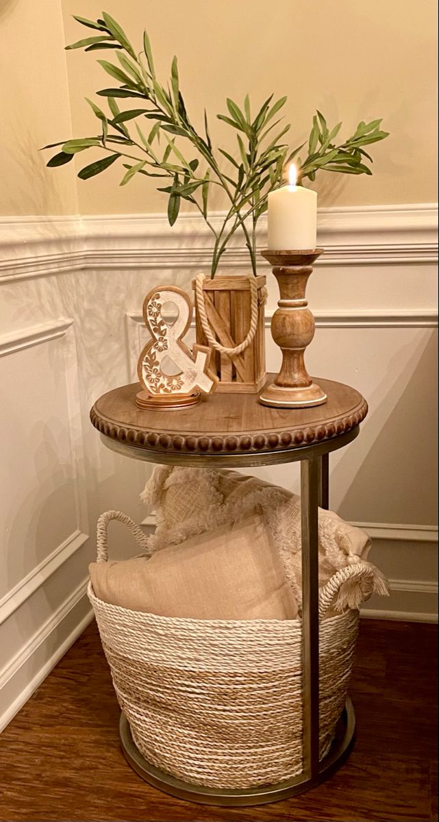 a small table with a vase and candles on it next to a basket filled with towels