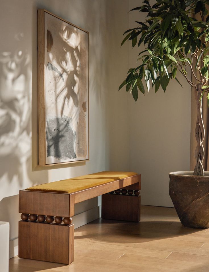 a wooden bench sitting next to a potted plant on top of a hard wood floor