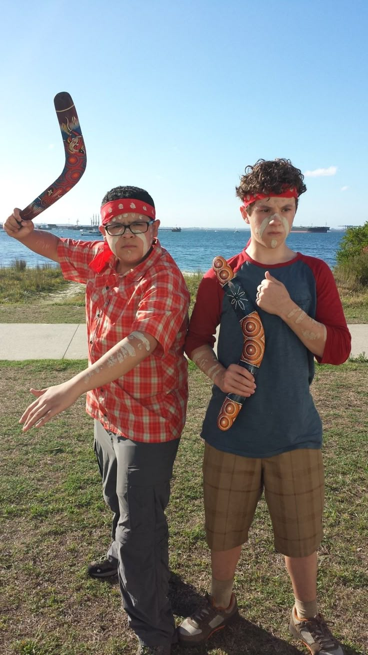 two people standing next to each other in the grass with one holding a skateboard