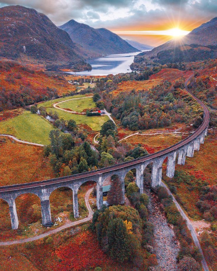 an aerial view of a train crossing over a bridge in the middle of mountains with trees and grass on both sides