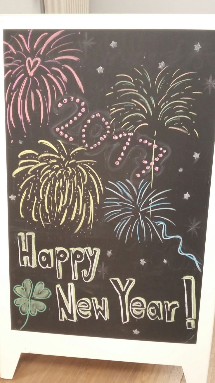 a chalkboard sign with fireworks and stars on it that says happy new year in front of a wooden floor