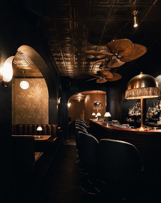 a dimly lit bar with several chairs and lamps on the wall, along with two ceiling fans